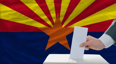 man putting ballot in a box during elections in front of flag american state of arizona