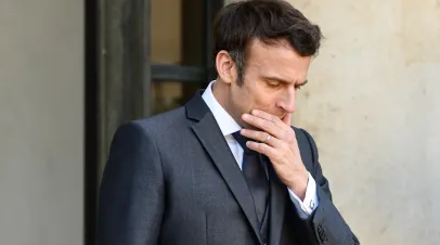 French President Macron walking with his hand over his mouth in frustration