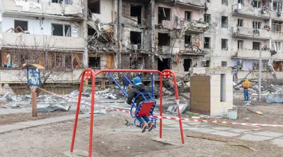 KYIV, UKRAINE - Feb. 25, 2022: War of Russia against Ukraine. Child on a swing against a residential building damaged by Russian rocket in a residential area of Kyiv.