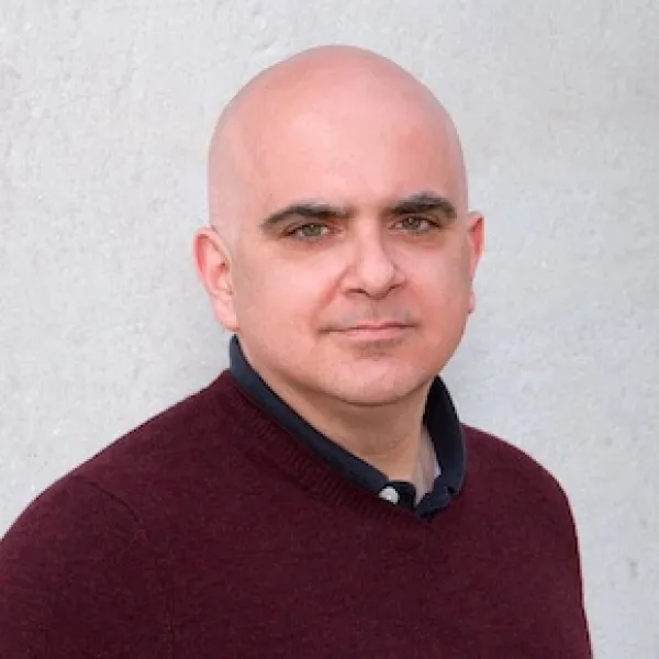 Bald man wearing a maroon sweater standing in front of a white background.