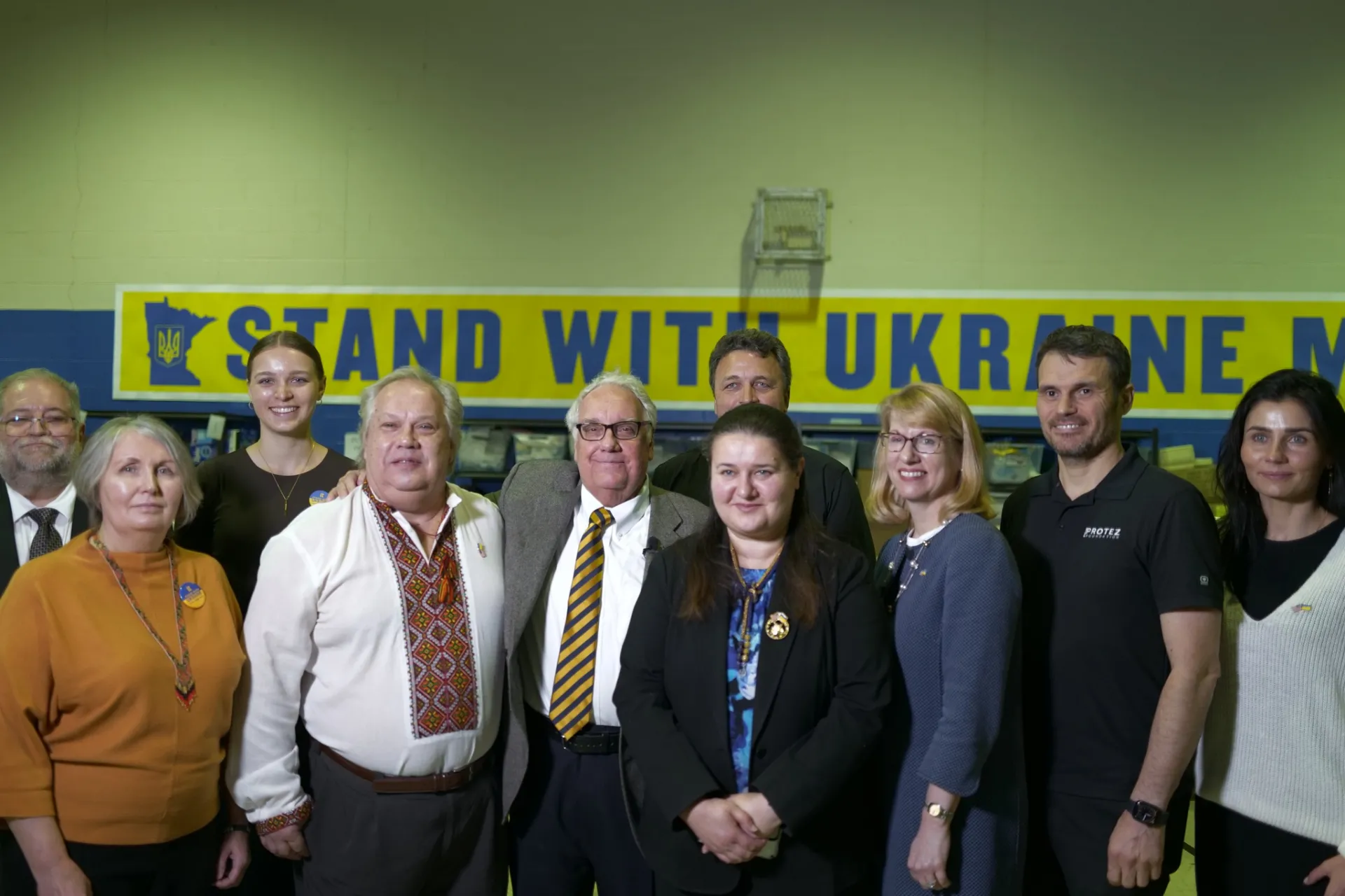 A group of people posed together with a banner reading "STAND WITH UKRAINE"