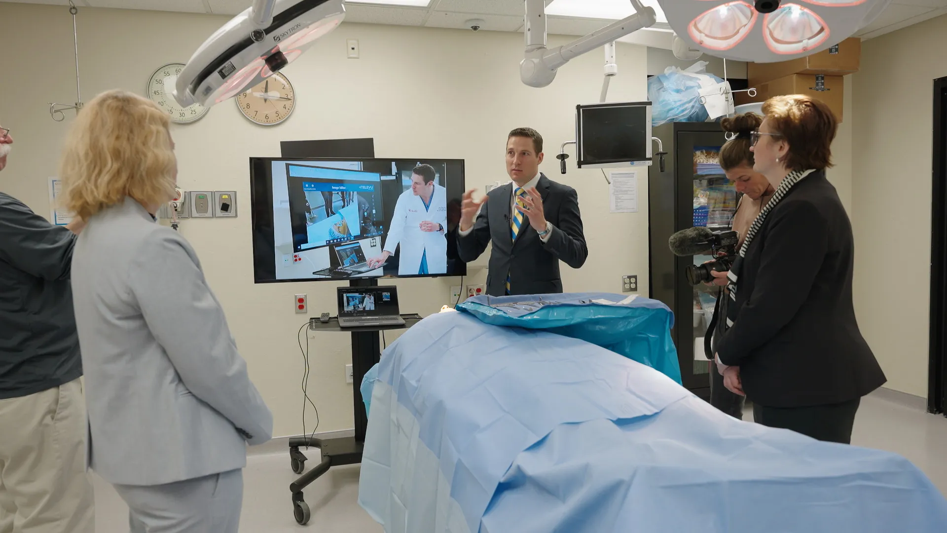 Three people standing around an training classroom for surgeon with a hospital bed in the center 