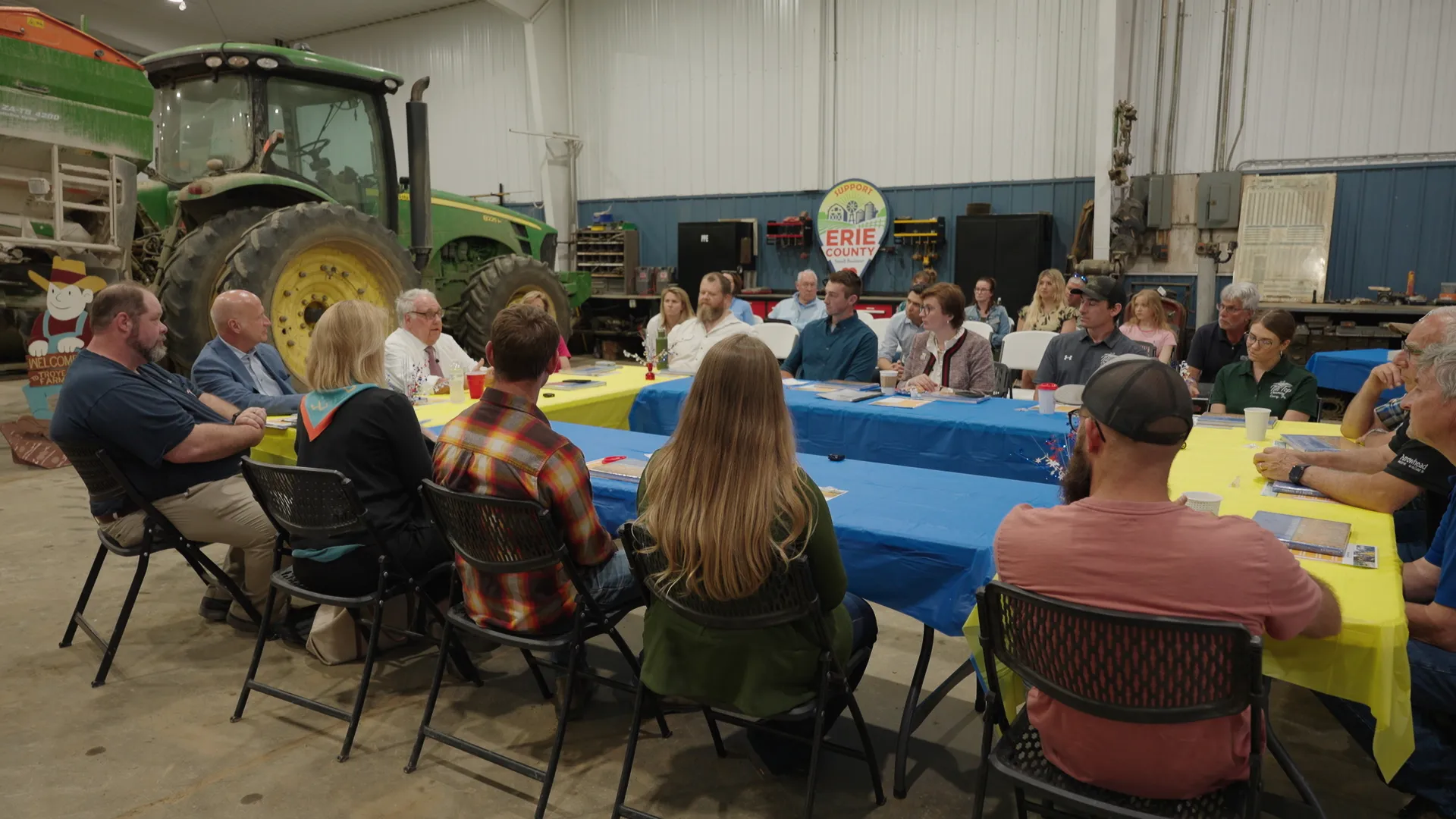 A group of people sitting around a circle of tables with a large tractor in the background